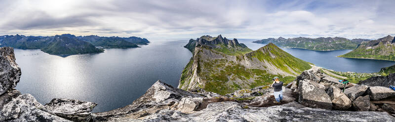 Man with camera photographing Hesten and Inste Kongen mountains standing on Segla peak, Senja island, Troms county, Norway, Scandinavia, Europe - RHPLF21418