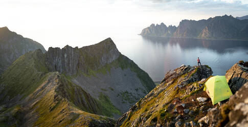 Tourist admiring sunset over the fjord out of camping tent, Senja island, Troms county, Norway, Scandinavia, Europe - RHPLF21427