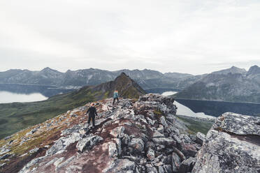 Two young women hikers climbing the rocks on Hesten Mountain peak, Senja, Troms county, Norway, Scandinavia, Europe - RHPLF21665