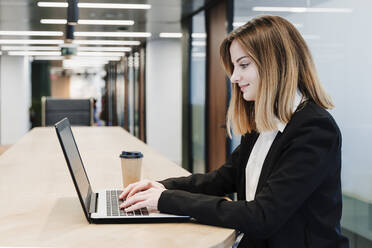 Smiling businesswoman using laptop on table in office - EBBF05462