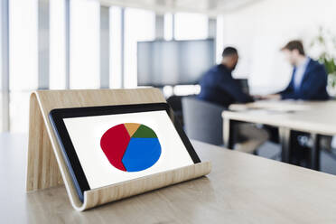 Tortendiagramm auf dem Display eines Tablet-PCs mit Geschäftsleuten im Hintergrund in einem Coworking-Büro - EBBF05500