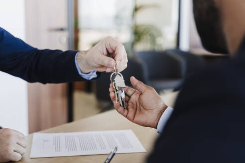 Immobilienmakler übergibt Hausschlüssel an Käufer im Büro - EBBF05502