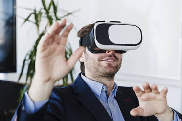 Businessman gesturing wearing virtual reality headset in office - EBBF05504