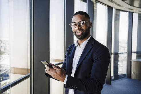 Smiling businessman with smart phone at office - EBBF05530