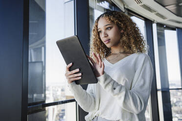 Geschäftsfrau mit lockigem Haar, die einen Tablet-PC im Büro benutzt - EBBF05554