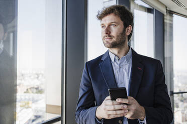 Thoughtful businessman with smart phone in office - EBBF05566