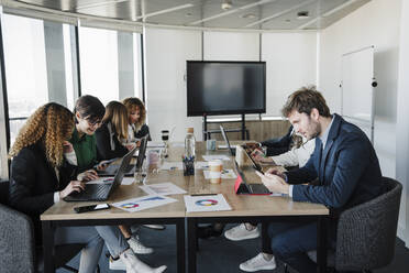 Multi-ethnic business colleagues working together at desk in coworking office - EBBF05573