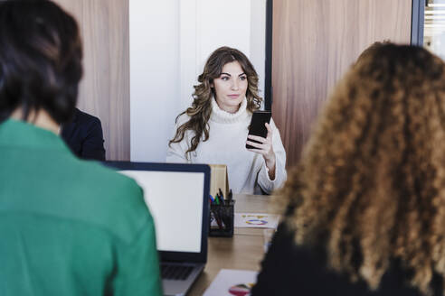 Geschäftsfrau mit Smartphone am Schreibtisch in einem Coworking-Büro - EBBF05582