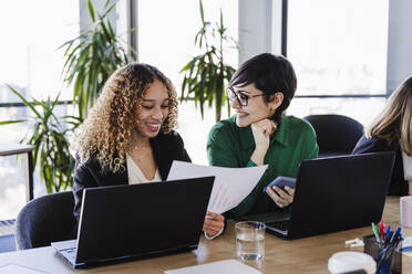 Glückliche Geschäftsfrauen, die mit Laptops am Schreibtisch in einem Coworking-Büro Finanzberichte prüfen - EBBF05584