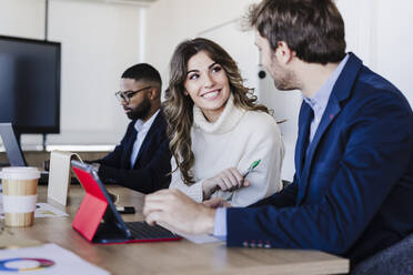 Lächelnde Geschäftsfrau, die mit einem Kollegen in einem Coworking-Büro diskutiert - EBBF05585