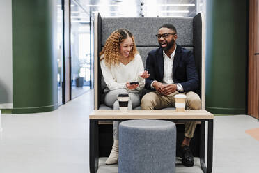 Glückliche Geschäftskollegen, die in der Kaffeepause in einem Coworking-Büro auf einem Stuhl sitzen - EBBF05602