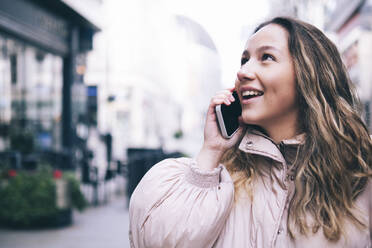 Lächelnde Frau, die auf der Straße mit einem Smartphone telefoniert - AMWF00169