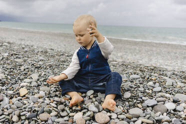 Blonder Junge spielt mit Kieselsteinen am Strand - SEAF00469