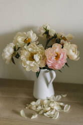 Verwelkte Pfingstrosen in Vase bei Blütenblättern auf dem Tisch - SEAF00484