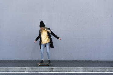 Frau auf dem Skateboard vor einer Mauer - GIOF14826