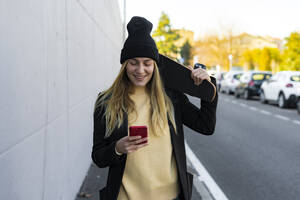 Smiling woman text messaging on smart phone on street - GIOF14830