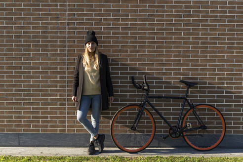 Junge Frau mit Fahrrad vor einer Backsteinmauer - GIOF14837