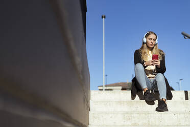 Young woman using smart phone sitting on steps - GIOF14844