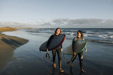 Frauen, die mit Surfbrettern in der Nähe des Meeres am Strand spazieren gehen, Gran Canaria, Kanarische Inseln - MRRF01892