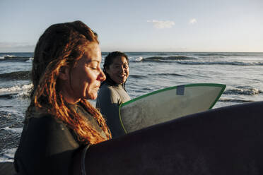 Lächelnde Frau betrachtet einen Surfer mit Surfbrett am Strand, Gran Canaria, Kanarische Inseln - MRRF01893