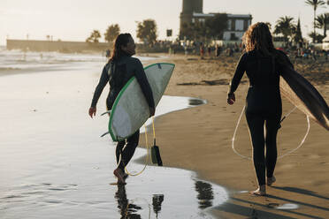 Surferinnen mit Surfbrettern gehen gemeinsam am Strand spazieren, Gran Canaria, Kanarische Inseln - MRRF01894