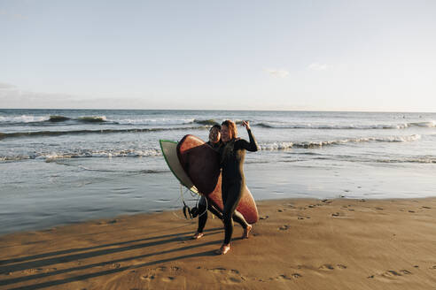 Fröhliche Surferinnen mit Surfbrettern, die am Strand spazieren gehen, Gran Canaria, Kanarische Inseln - MRRF01899