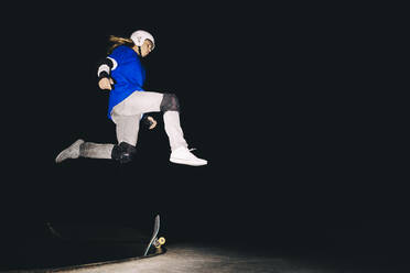 Skateboarder jumping over skateboard at night - OMIF00577