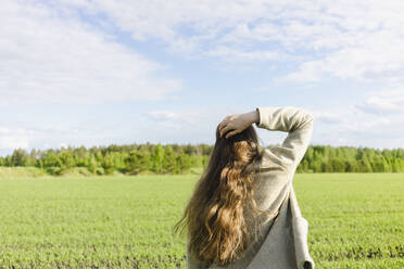 Junge Frau mit Hand im Haar auf einer grünen Wiese an einem sonnigen Tag - SEAF00485