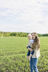 Mother with eyes closed hugging son at green field - SEAF00486