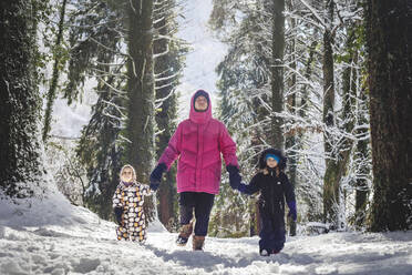 Vater mit Töchtern beim Spaziergang im verschneiten Wald an einem sonnigen Tag - OMIF00586
