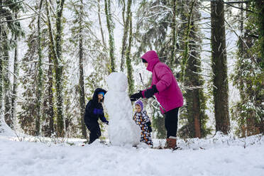 Vater mit Töchtern baut Schneemann im Winterwald - OMIF00595