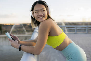 Smiling woman with smart phone listening music on headphones - JCCMF05272