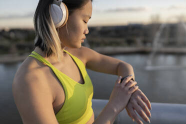 Young athlete with headphones checking time on wristwatch - JCCMF05273