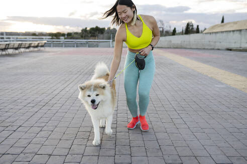 Lächelnde Sportlerin mit Hund auf dem Gehweg - JCCMF05277