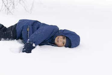 Niedlicher Junge in Jacke auf Schnee liegend im Winter - SEAF00498