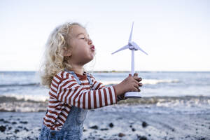 Boy blowing wind turbine toy at beach - ASGF02112
