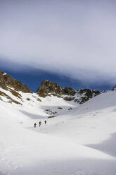 Ski mountaineerers walking on snow towards mountain at Orobic Alps in Valtellina, Italy - MCVF00950