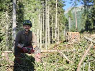 Lächelnder Holzfäller sitzt auf einem umgestürzten Baum im Wald - CVF01910