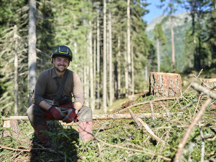 Lächelnder Holzfäller sitzt auf einem umgestürzten Baum im Wald - CVF01910