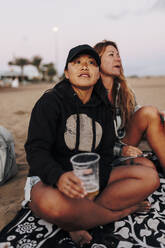 Nachdenkliche Frau mit Bierbecher bei einem Freund am Strand sitzend - MRRF01923