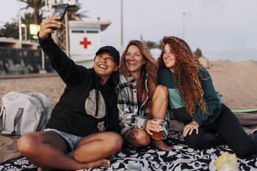 Lächelnde gemischtrassige Freunde machen ein Selfie mit ihrem Smartphone am Strand - MRRF01924