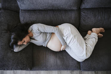 Pregnant woman lying on sofa at home - EBBF05624