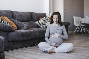 Schwangere Frau sitzt im Schneidersitz zu Hause - EBBF05635
