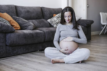 Smiling pregnant woman sitting on floor at home - EBBF05639