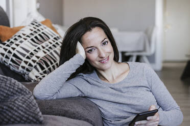 Smiling woman with smart phone leaning on sofa at home - EBBF05641