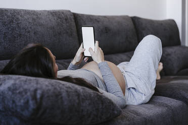 Pregnant woman using smart phone on sofa at home - EBBF05652