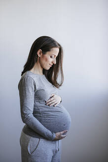 Schwangere Frau vor einer Wand stehend - EBBF05657
