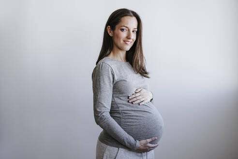 Schwangere Frau mit Bauch vor einer Wand stehend - EBBF05658