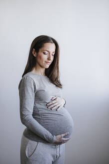 Schwangere Frau mit geschlossenen Augen vor einer Wand stehend - EBBF05659