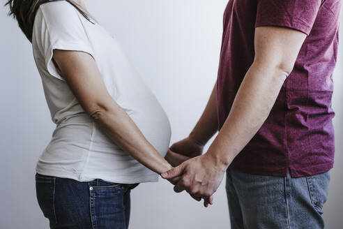 Pregnant woman with man holding hands in front of wall - EBBF05664